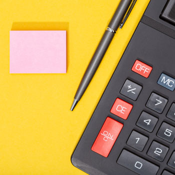 calculator-pen-and-blank-sticky-note-on-yellow-bac-XDB2VVF